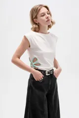 Remera de poliéster color blanco, de corte ajustado, con cuello bote, mangas sisa y detalles de aberturas (cut-out) en los costados con apliques florales en tono celeste.