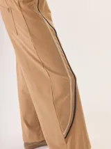 Pantalón de corte ancho y estilo comfy, confeccionado en algodón color marrón. Presenta detalles de franjas verticales en tonos beige y rojo a lo largo de las piernas, con cintura elástica.