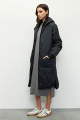 Campera de nylon larga oversized color negro, con capucha, tres bolsillos externos y uno interno. De tela capitoneada, con puños en las mangas y forro polar.