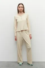 Conjunto de pijama color beige, compuesto por una remera de manga larga con botones en el escote y un pantalón de corte recto con cintura elastizada y cordón ajustable.