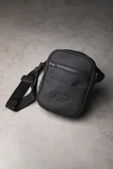 Mini morral de material engomado color negro, con compartimento principal y bolsillos frontales (uno de ellos con cierre). Cuenta con correa ajustable y logo en relieve.