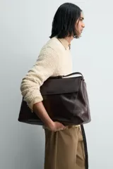 Bolso bandolera de piel color marrón oscuro, con solapa y cierre de imán y cremallera. Incluye un bolsillo interior con cremallera y un bolsillo plano. Tiene asa de hombro ajustable.