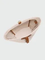 Cartera tipo bucket de tamaño pequeño, confeccionada en lona color crudo con detalles en cuero color tostado. Presenta una base redondeada, cierre de solapa con broche y correa ajustable para llevar al hombro.