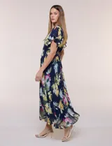 Vestido midi azul marino con estampado floral multicolor, confeccionado en gasa liviana con falda plisada. Tiene escote en V, mangas cortas estilo mariposa y lazo ajustable en la cintura.