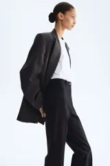Pantalón negro de corte bootcut, con tiro alto, trabillas para cinturón y cierre frontal con botón y cremallera. Cuenta con pliegues marcados al frente y bolsillos simulados con solapa en la parte delantera.