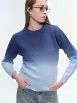 Buzo tejido de punto con diseño degradé que transiciona de azul oscuro a celeste claro. Presenta cuello redondo, mangas largas y puños acanalados, con un corte holgado y relajado.