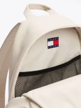 Mochila Tommy Jeans color crema, de poliuretano, con cierre de cremallera, asa superior y correas ajustables y acolchadas. Tiene un compartimento principal, un bolsillo interior de malla y un bolsillo exterior con cremallera.