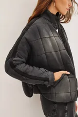Campera acolchada de corte holgado con diseño de costuras cuadradas, cierre frontal con cremallera y cuello alto. Presenta un acabado lavado en tonos gris y negro.