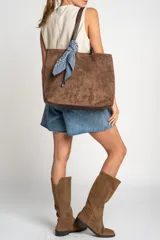Bolso tipo tote de gran tamaño en color camel, confeccionado en cuero vegano con acabado efecto gamuza. Presenta doble asa larga para llevar al hombro y una placa metálica pequeña con el logo de la marca en el frente.