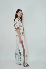 Pantalón de lino color celeste claro, de corte holgado y pierna recta. Presenta una franja lateral decorativa con estampado geométrico y detalles de palmeras estampadas en la parte inferior de las piernas.