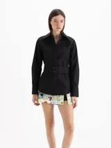 Camisa Oslo de poplín negro, confeccionada con mezcla de poliéster y algodón. Cuenta con silueta estructurada, cuello camisero amplio y cierre frontal oculto. Incorpora un cinturón ancho ajustable con hebilla rectangular forrada y ojalillos metálicos.