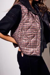 Chaleco negro con cierre frontal y cuello alto, de corte al cuerpo y diseño acolchado. Reversible, con interior a cuadros.