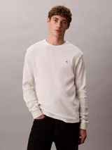 Remera de manga larga Calvin Klein de color blanco off-white, confeccionada en tejido de punto térmico con textura de nido de abeja. Presenta cuello redondo, puños acanalados y un pequeño logo bordado en el pecho.