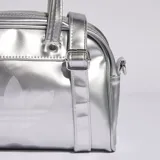 Mini bolso estilo bowling Adidas Adicolor plateado con acabado metalizado, asas de mano y correa desmontable. Presenta el logotipo del Trifolio grabado en la parte frontal.