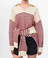 Chaleco de punto color marfil con cuello polo, escote en V y diseño de rayas horizontales burdeos en el pecho y las mangas. Cuenta con mangas largas y un diseño holgado, ideal para usar superpuesto o anudado.