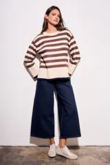 Sweater de punto a rayas horizontales negras y crudas, con cuello redondo y mangas largas. Tiene ribete marrón en puños y ruedo.