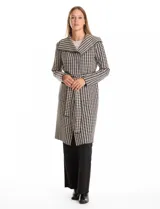 Chaqueta larga de tejido de punto con estampado de pata de gallo en blanco y negro. Presenta cuello de solapa, cierre frontal con lazo ajustable en la cintura y bolsillos aplicados en el frente.