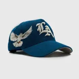 Gorra tipo baseball de pana color azul, con bordado frontal en tipografía gótica y bordado lateral de una paloma. Cuenta con ajuste posterior.