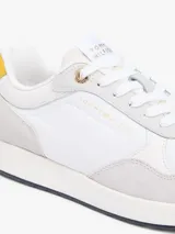 Zapatillas de estilo runner de Tommy Hilfiger, confeccionadas en una mezcla de cuero y textil en color blanco con detalles en gris claro y un panel amarillo en el talón. Presentan cordones blancos y suela de goma con base oscura.