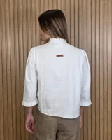 Camisa de algodón color blanco con rayas verticales rosadas, cuello alto con volados, mangas tres cuartos abullonadas con puños elastizados con volados y cierre frontal de botones oscuros.