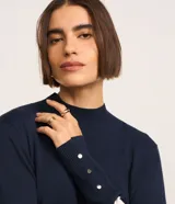 Blusa alargada de punto con diseño rayado horizontal en azul marino y blanco, cuello alto y manga larga con detalles de botones en los puños.