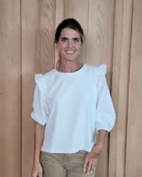 Remera blanca de algodón con cuello redondo, mangas tres cuartos abullonadas y detalle de volados en los hombros.