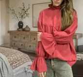 Blusa color beige de corte holgado, cuello alto con volados y mangas largas abullonadas con elástico en los puños.