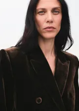 Blazer de terciopelo color marrón oscuro, con cuello de solapa, cierre frontal de doble botonadura y bolsillos con solapa. Presenta un diseño recto y forro interior.