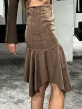 Falda midi color marrón con textura plisada, diseño de corte asimétrico con volado en el ruedo y ajuste lateral con cierre.