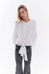 Camisa blanca de lino italiano, de corte holgado, mangas largas abullonadas, cuello mao y cierre frontal con botones, con diseño para anudar en la cintura.