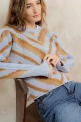 Sweater de punto jacquard con diseño de chevron en tonos celeste y marrón. Presenta cuello redondo, corte holgado y mangas largas con hombros abullonados.