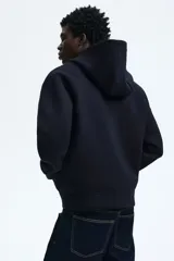 Campera con capucha de tejido efecto neopreno, con cierre frontal completo, hombros caídos y bolsillos delanteros abiertos. Presenta un corte holgado y diseño minimalista.