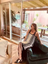 Vestido largo tejido en lurex color beige con diseño vertical y terminación en flecos negros. Breteles finos de cuero intervenido a mano con tientos de cuero plateado.