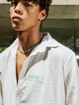 Camisa de lino con diseño de cuadrillé en tonos blanco y beige, de manga larga y cuello clásico. Presenta una pequeña estampa en el pecho y una estampa en la espalda, con un calce holgado y relajado.