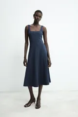 Vestido midi de color beige con escote cuadrado y tirantes anchos. Presenta un diseño entallado en el torso con costuras verticales marcadas y falda con caída evasé.