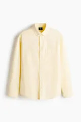 Camisa H&M de algodón Oxford en color amarillo claro, con cuello americano, bolsillo en el pecho y cierre frontal con botones.