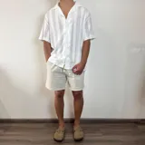 Camisa de tejido calado con textura, color blanco, de corte oversize, manga corta y cuello solapa con cierre frontal de botones.
