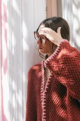 Saco oversize de tejido de punto en color beige, con mangas caídas y detalles de bordado a mano en tonos verde y lila en los bordes y costuras.