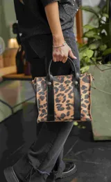 Cartera mini tipo tote bag con estampado animal print, doble asa corta de cuero sintético negro y cierre superior.