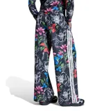 Pantalón deportivo Adidas modelo Farm Tiro para mujer, de corte holgado y diseño estampado con flores y hojas sobre fondo negro. Cuenta con cintura elástica y las clásicas tres tiras blancas a los lados.
