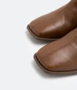 Bota de cuero de caña media para mujer, con punta cuadrada y tacón bloque de 6 cm. Presenta un cierre de cremallera en el lateral interno y una costura central decorativa en la parte frontal.