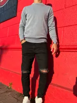 Pantalón chupín de jean color negro, de corte ajustado y diseño con roturas en las rodillas.