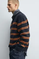 Jersey de punto con ajuste relajado, cuello redondo y manga larga. Presenta un diseño de rayas horizontales en color naranja sobre una base de color azul marino, con acabados en rib en puños, cuello y ruedo.