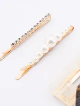 Set de tres pinzas para el pelo. Incluye una horquilla fina con strass, una horquilla con perlas sintéticas y una pinza rectangular grande con diseño de mármol en tonos negro y beige con detalles dorados.