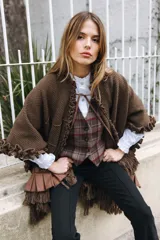 Ruana de punto color marrón con textura marcada, cuello con volado y lazo frontal regulable. Presenta terminaciones con volados de lino en mangas y ruedo, además de flecos decorativos en la parte inferior.