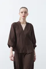 Blusa de manga larga color marrón oscuro, con escote en V y cuello mao. Presenta frunces en el canesú y puños ajustados.