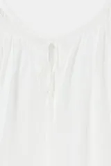 Blusa de lino color amarillo pastel, con escote recto ajustable mediante lazadas, hombros descubiertos y mangas largas abullonadas con puños elásticos.