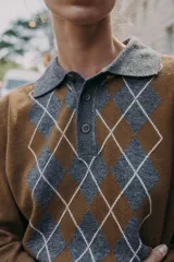Jersey de punto con cuello polo y cierre frontal de botones. Presenta un diseño de estampado de rombos en el frente en tonos gris y blanco sobre una base color marrón.