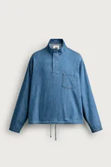 Camisa polo de corte relajado confeccionada en denim ligero de algodón con efecto lavado. Presenta cuello subido, cierre frontal con botonadura oculta por solapa, manga larga, bolsillo de plastrón en el pecho y bajo ajustable con cordón.