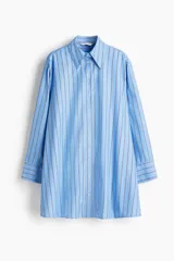 Vestido camisero corto de corte evasé y diseño oversize, color celeste con estampado de rayas verticales finas. Cuenta con cuello clásico de solapa, cierre frontal de botones, hombros caídos y mangas largas con puños abotonados.